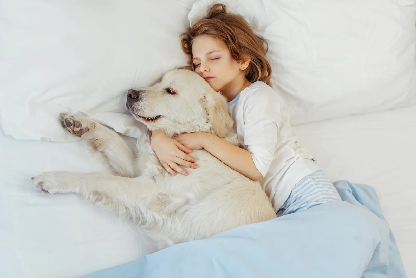 Child hugging a golden retriever in a bed